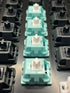 Vijf KTT Mint switches gemonteerd op een toetsenbord tussen zwarte switches – bovenaanzicht